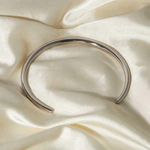 Detailed close-up of a silver minimalist open cuff bracelet on elegant beige silk fabric