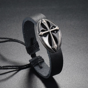 Macro detail of braided black leather bracelet with an antique silver cross charm