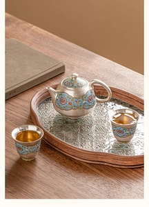 Detailed close-up of a silver-plated enamel tea set with blue floral motifs on a wooden tray