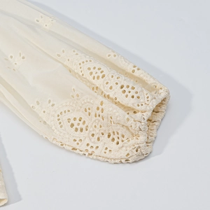 Detailed close-up of hollow floral embroidery on cream-colored cotton sleeve cuff
