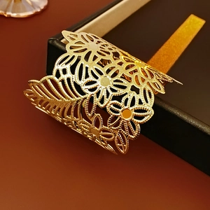 Detail of a wide gold open cuff bracelet with intricate laser-cut floral patterns