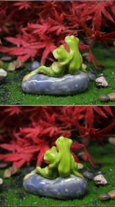 Detail of cute couple frogs sitting on a gray pebble for garden bonsai decoration