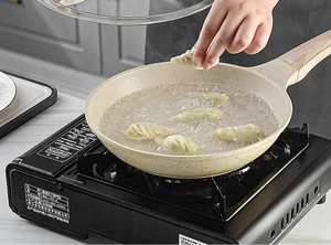 Close-up of a beige maifan stone non-stick frying pan boiling dumplings on a gas stove