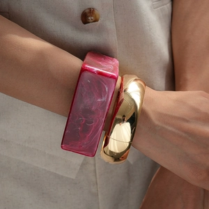 Close-up of stacked pink marble resin bangle and polished gold wide metal bracelet