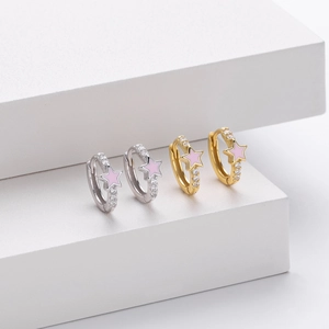 Macro detail of gold and silver earrings with pink star enamel and white zircon stones