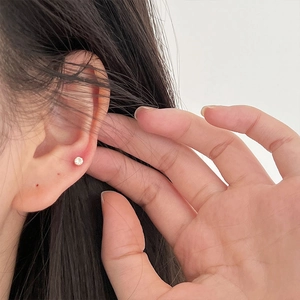 Close-up of golden four-prong zircon stud earring on a female ear model with clean background
