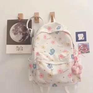 Detailed view of the cute floral print and plush flower pendant on the white backpack