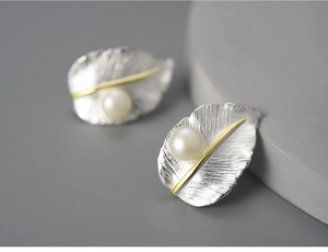 Macro shot of silver leaf earrings with gold veins and centered white pearls