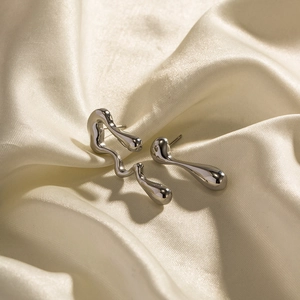 Macro detail of silver fluid irregular earrings on premium champagne silk fabric