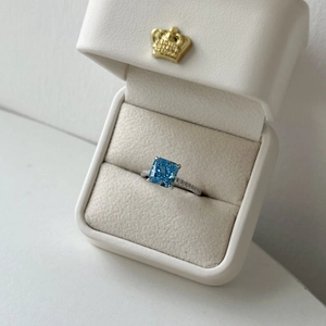 Detailed view of square blue zircon ring with small side diamonds in a white jewelry box