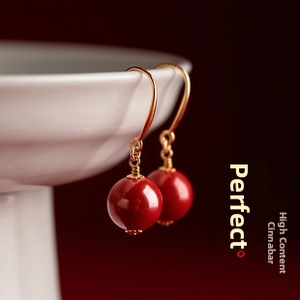 Macro shot of high-content cinnabar red bead earrings with golden hooks on white porcelain