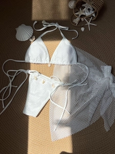Three-piece white mesh bikini set with natural shell charms on a rustic beach mat