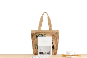 Détail d'un sac cabas tissé beige avec lettrage brodé vert sur une table en bois