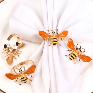 Golden and yellow enamel bee napkin rings set on white ceramic plate with napkins