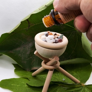 Detailed macro of essential oil being dropped into a wooden aroma diffuser bowl with stones