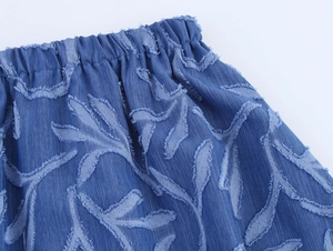Detail of blue denim skirt with elastic waist and jacquard leaf pattern with frayed edges