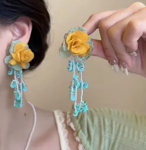 Detailed view of yellow rose tassel earrings with fabric petals and green bead strands