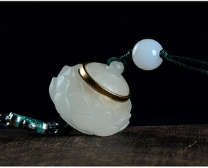 Detailed close-up of a white carved lotus seed pod pendant with brass ring and green cord