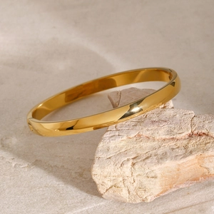 Close-up of a polished gold stainless steel bangle resting on a textured stone surface