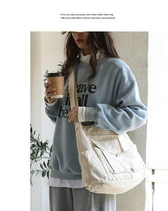 Detail of multi-pocket off-white canvas messenger bag styled with light blue sweatshirt