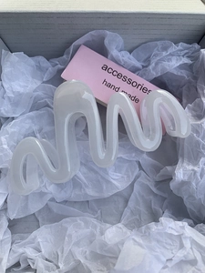 Macro shot of wavy creamy white resin hair claw clip on minimalist packaging paper