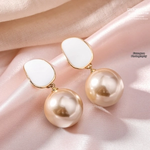 Gros plan de boucles d'oreilles perles champagne et émail sur fond de satin rose doux