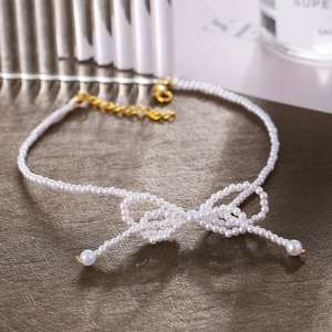 Macro shot of pearl choker featuring an intricate woven bow pendant and gold clasp