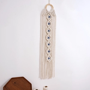 Detailed view of woven cotton tapestry with blue evil eye beads and soft fringe