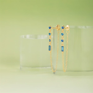 Detail of S925 silver gold tassel earrings with blue zircon on glass display