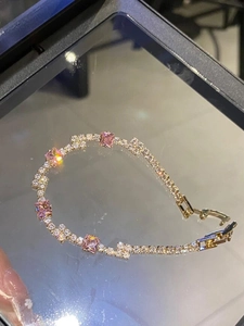 Detail of gold tennis bracelet with white round zircons and pink square gemstones