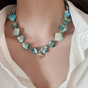 Close-up of bohemian shell necklace with teal beads and golden scallop pendant