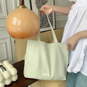 Detail of light green canvas tote bag with Senzhhi brand label shown in a lifestyle setting