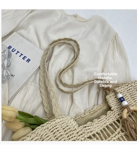 Detail of beige straw tote bag featuring wavy edges and blue evil eye bead charm