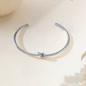 Minimalist silver knot bangle in stainless steel with open-cuff design on beige background