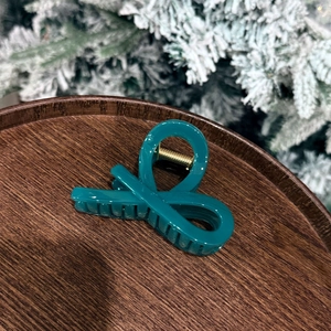 Detail of teal bow hair claw clip with golden spring on dark wooden tray over snowy background