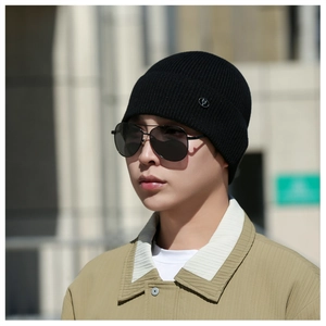 Detailed texture of black ribbed knit beanie with silver round metal logo accent