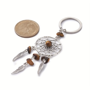 Detail of dreamcatcher keychain with tiger eye stone and metal feathers next to a coin