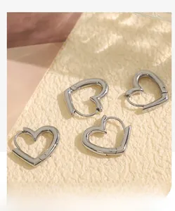 Detailed view of two pairs of heart-shaped silver hoop earrings on a textured background