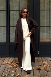Detailed view of women's long brown coat with cream knit cardigan and matching wide trousers
