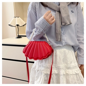 Detail of red shell-shaped bag with pearl handle and crossbody strap worn by a model
