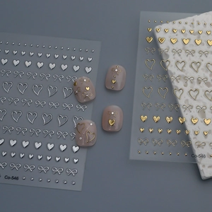 Golden and silver 3D nail art stickers with metallic bows and hearts on grey background