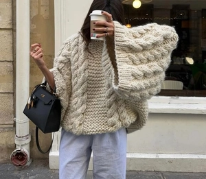 Close-up of beige oversized chunky cable knit sweater with drop shoulder and relaxed fit