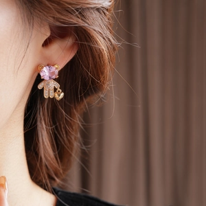 Close-up of asymmetrical bear and heart earrings with pink gems on a female model