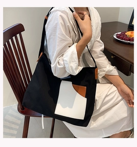 Detail of a black canvas tote bag with contrast pocket held by a model in a natural setting