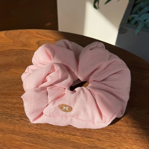Detail view of pink cotton oversized scrunchie with bow emblem on a dark wood table