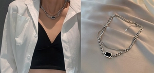 Detail of layered silver chain necklace with black rectangular pendant on beige fabric