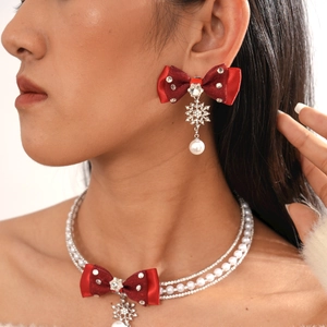 Detail of layered Christmas necklace featuring red bows, snowflakes and pearls on model
