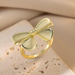Minimalist golden bow open ring displayed on natural beige stone with soft fabric