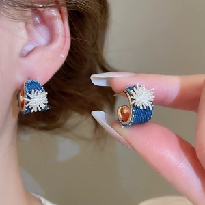 Close-up of C-shaped blue denim earrings with gold metal frame and white floral star pattern
