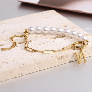 Close-up of pearl and gold paperclip chain bracelet with a metal letter M pendant